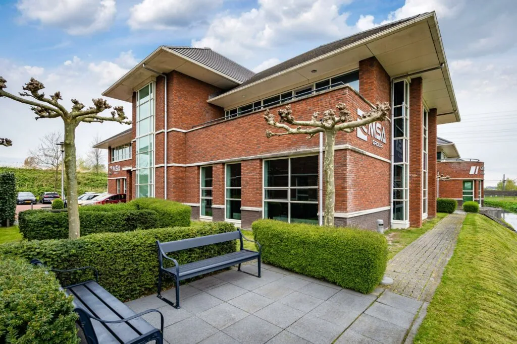 Modern kantoorpand aan de 1e Barendrechtseweg met rode bakstenen gevel, grote ramen en verzorgde groenvoorziening.